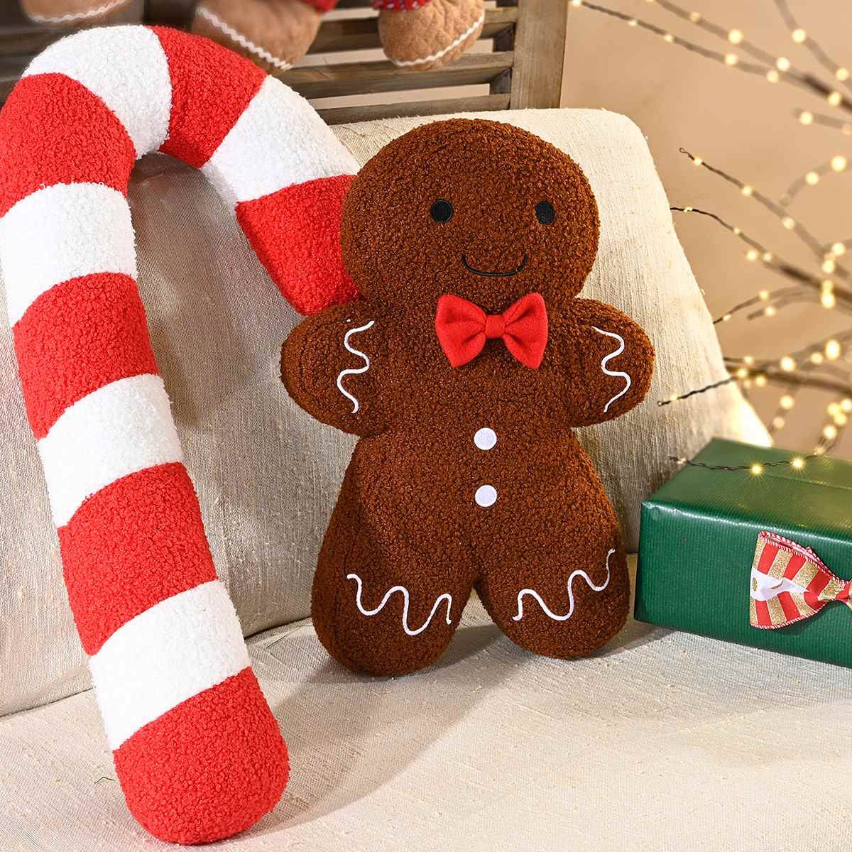 I due cuscini appoggiati a un divano beige, accanto a un regalo verde e a un ramo di luci