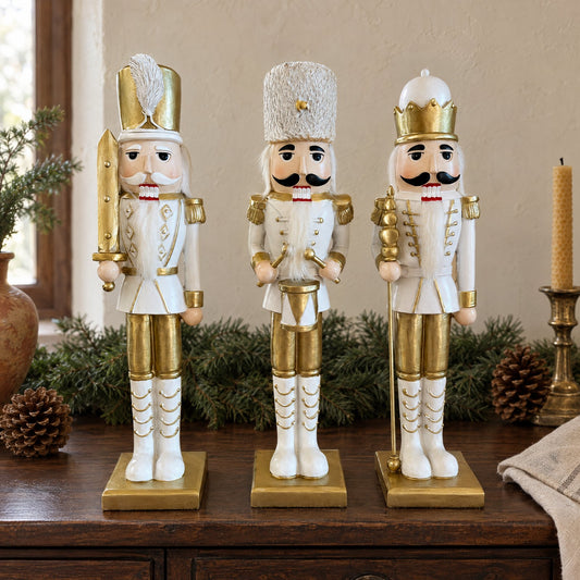 I tre schiaccianoci bianchi e oro in fila su una credenza di legno scuro, fra una ghirlanda di abete, pigne e un candeliere di ottone